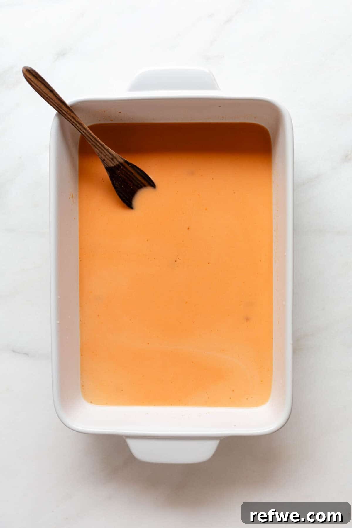Sheet Pan Dumpling Bake 4 Close-up of vibrant red curry sauce being mixed in a white baking dish.