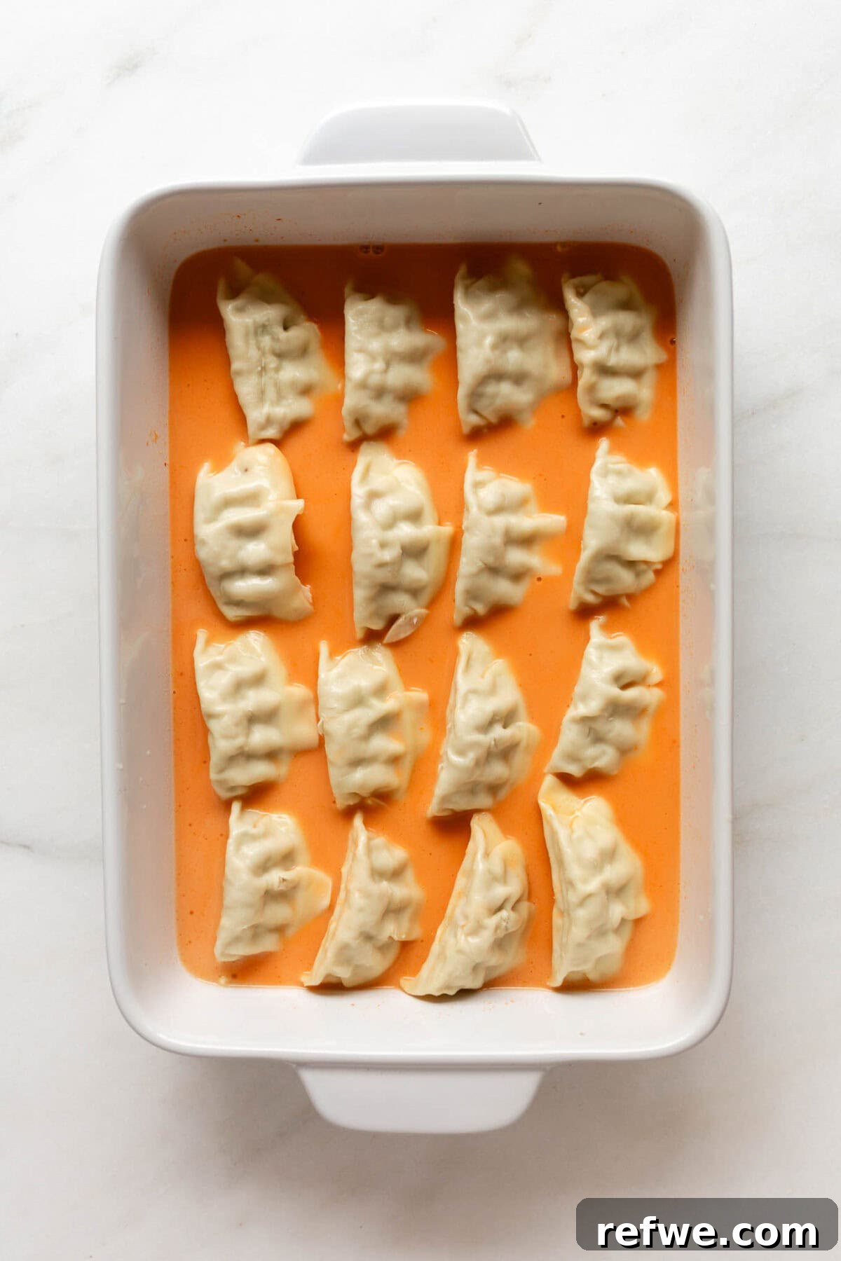 Sheet Pan Dumpling Bake 5 Unbaked dumplings carefully arranged in a baking dish, surrounded by the creamy red curry sauce.