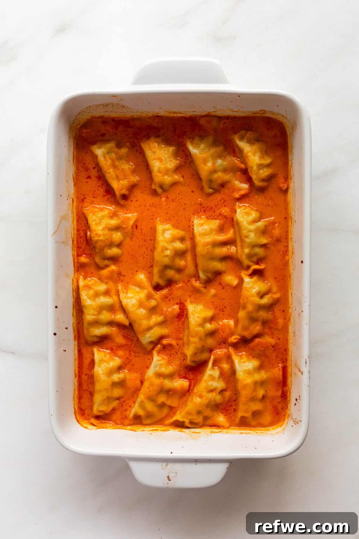 Sheet Pan Dumpling Bake 6 Freshly baked dumplings simmering in a vibrant red curry sauce in a white baking dish, ready to be served.