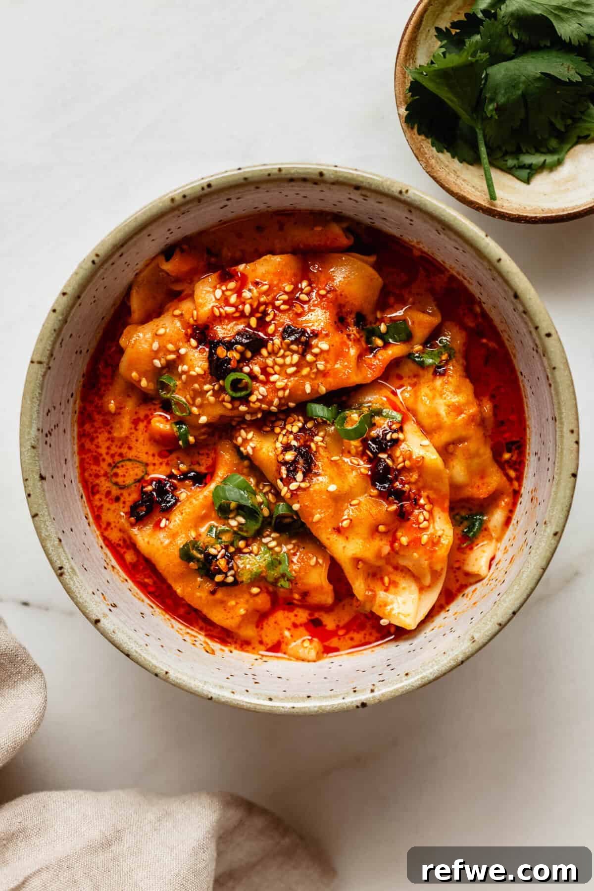 Sheet Pan Dumpling Bake 7 A serving of baked red curry dumplings topped with fresh cilantro in a bowl, with a separate small bowl of cilantro nearby.