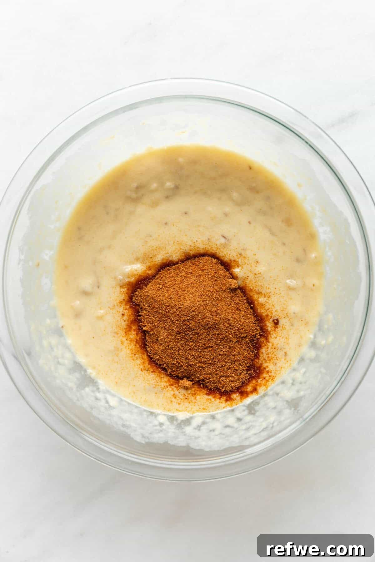 The mashed banana, egg, and yogurt mixture with coconut sugar being stirred into the bowl, creating a unified wet base.