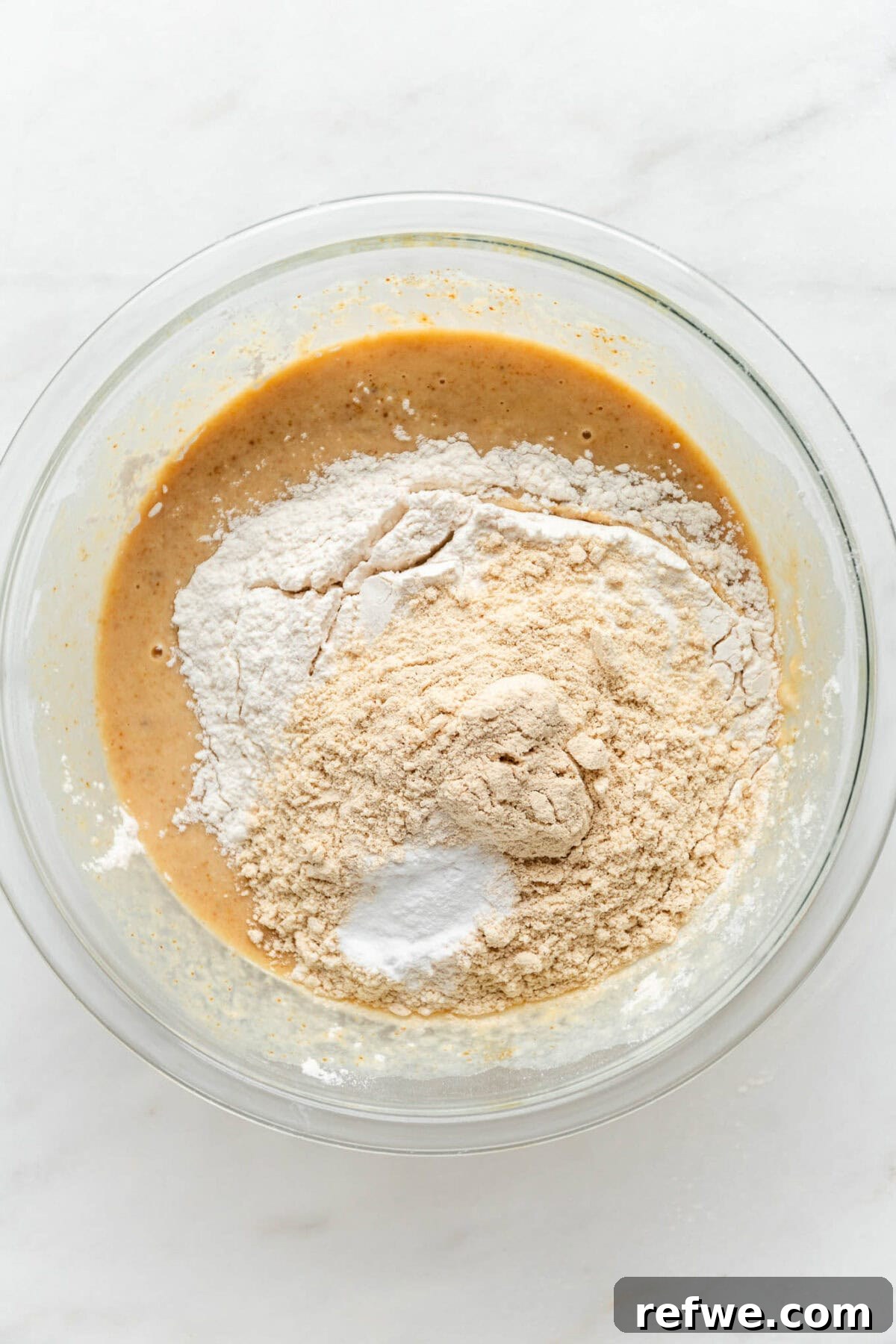 All wet and dry ingredients for banana muffins now together in a clear mixing bowl, ready for a final gentle mix.