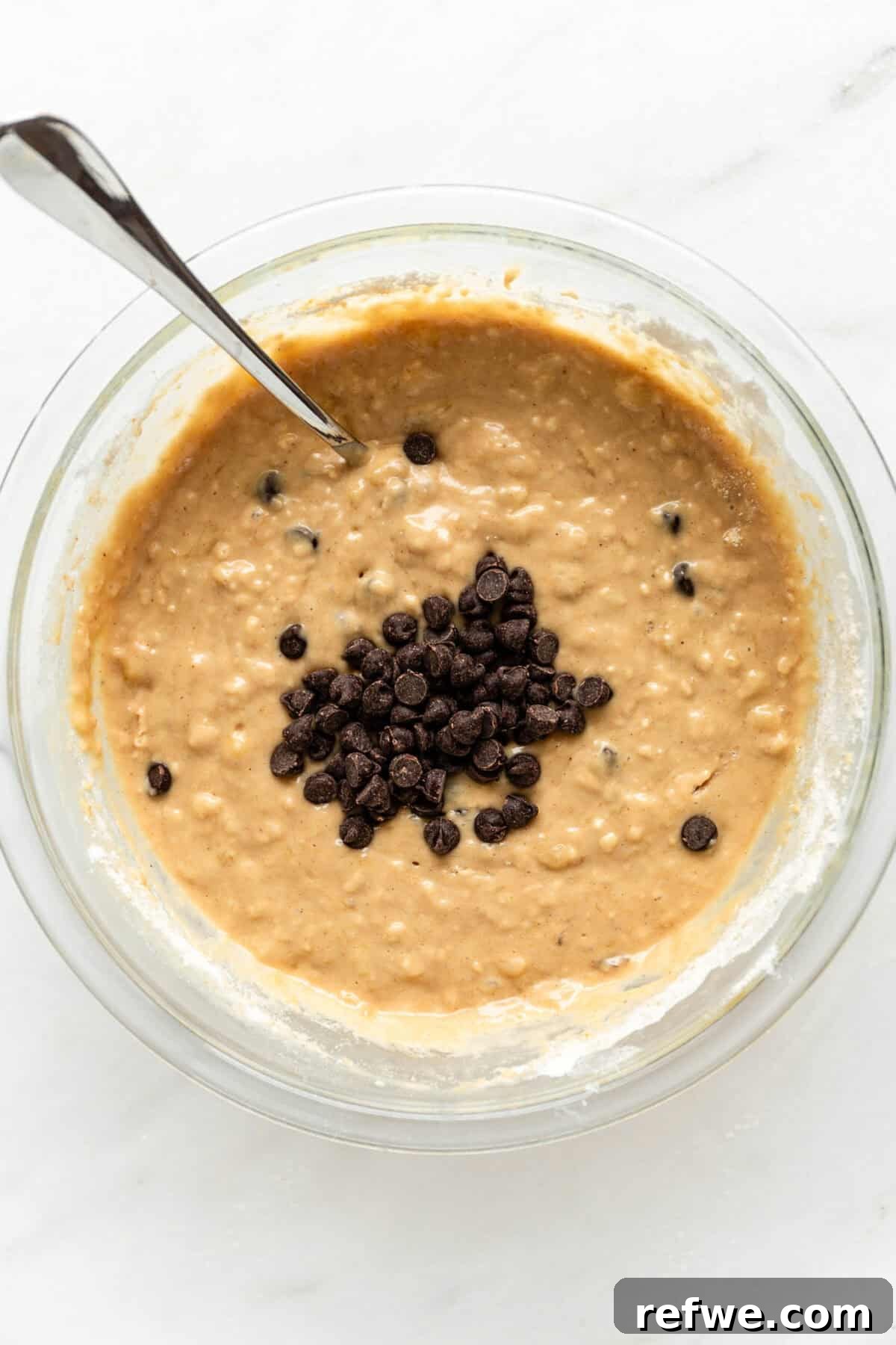 Banana muffin batter in a bowl, now beautifully studded with chocolate chips, ready for pouring.