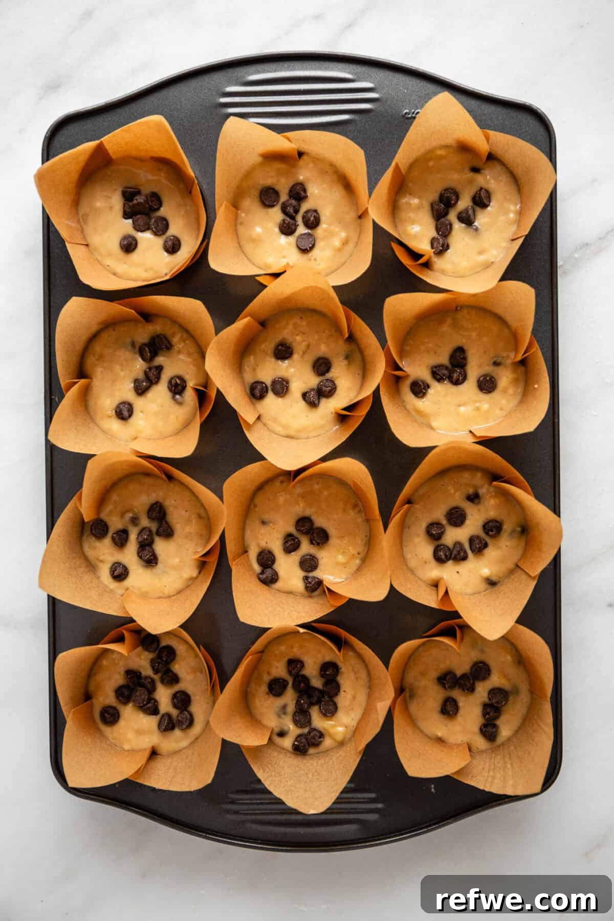 A muffin pan filled with unbaked banana chocolate chip muffin batter, waiting to go into the oven.