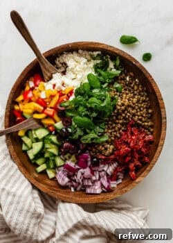 Mediterranean lentil salad in a wood bowl with wood spoons and a napkin on the side.