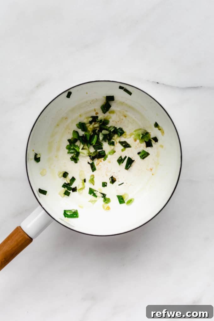 Peanut Butter Noodle Bliss 4 A white pot containing finely chopped green onions and minced garlic gently sautéing in oil, releasing an aromatic fragrance.