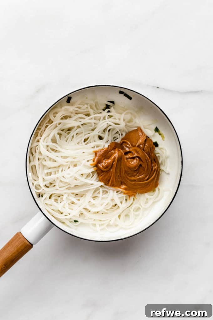 Peanut Butter Noodle Bliss 6 Cooked rice noodles and creamy peanut butter sauce glistening in a white pot, poised for mixing.