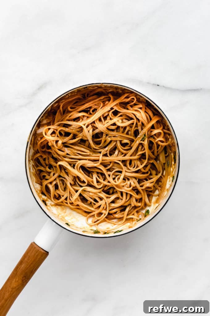 Peanut Butter Noodle Bliss 7 The finished peanut butter noodles, beautifully coated in sauce, being tossed in a white pot with a wooden handle.