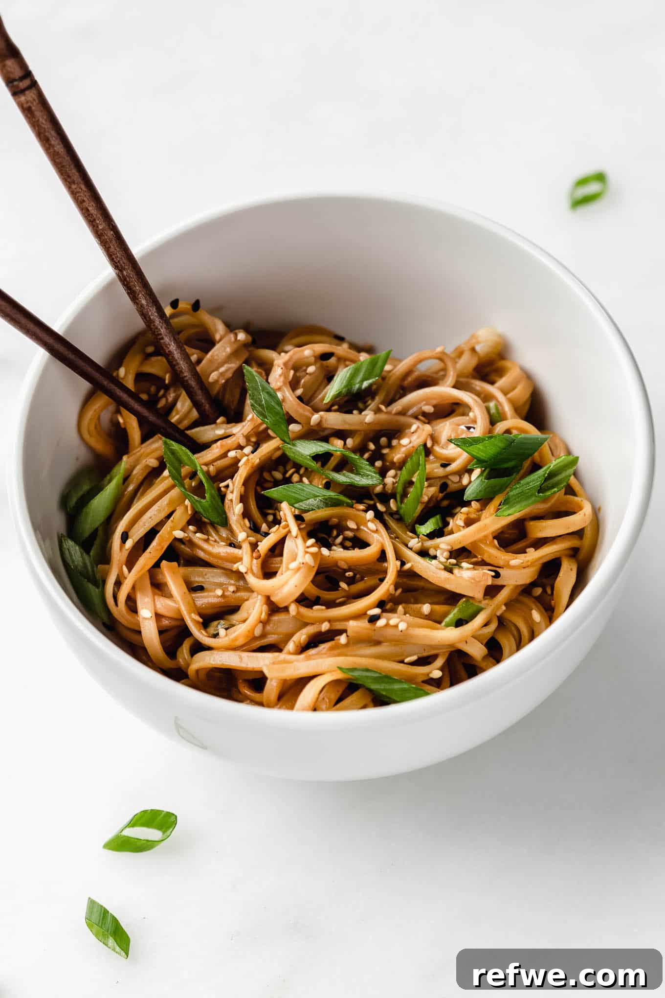 Peanut Butter Noodle Bliss 8 A close-up shot of creamy peanut butter noodles in a white bowl, generously topped with thinly sliced green onions and a sprinkle of sesame seeds, ready to be enjoyed.