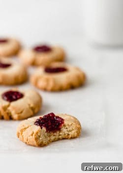 A vegan raspberry thumbprint cookie with a bite taken out of it on a marble counter