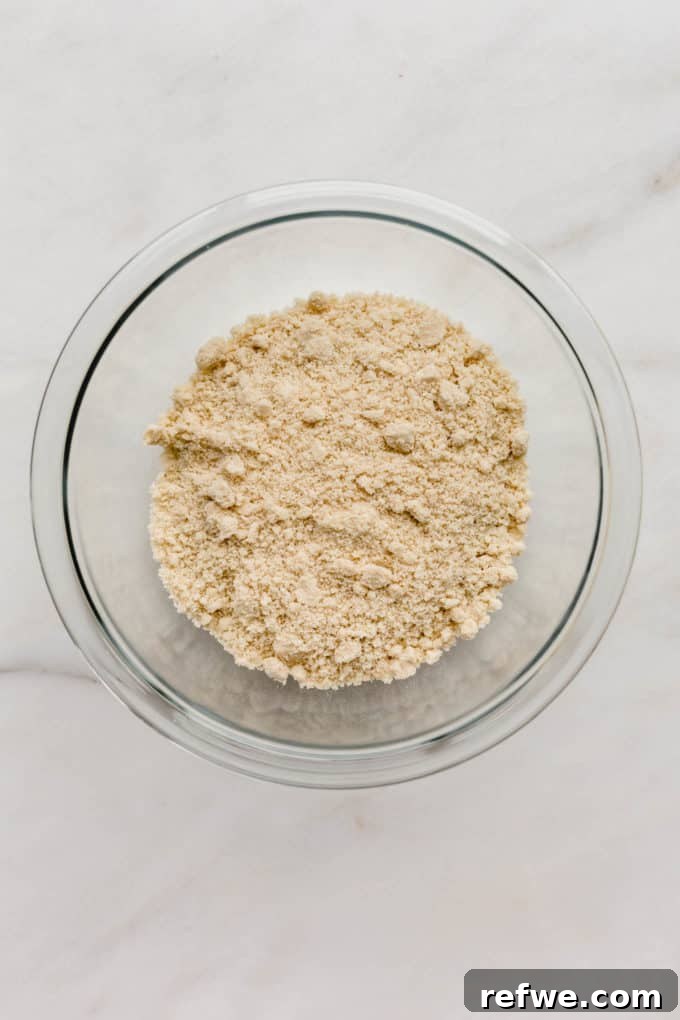 A clear mixing bowl filled with fine almond flour, illustrating the dry ingredients ready for combination.