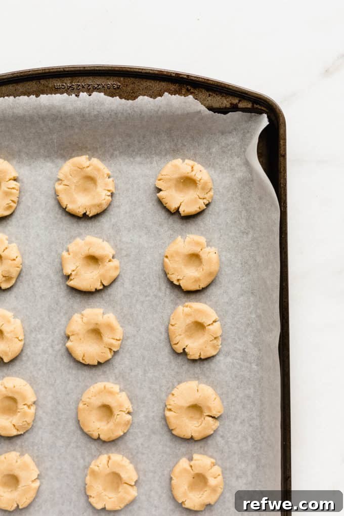 Raw thumbprint cookies on a baking sheet, with the indentations ready for jam, showcasing their perfect formation.