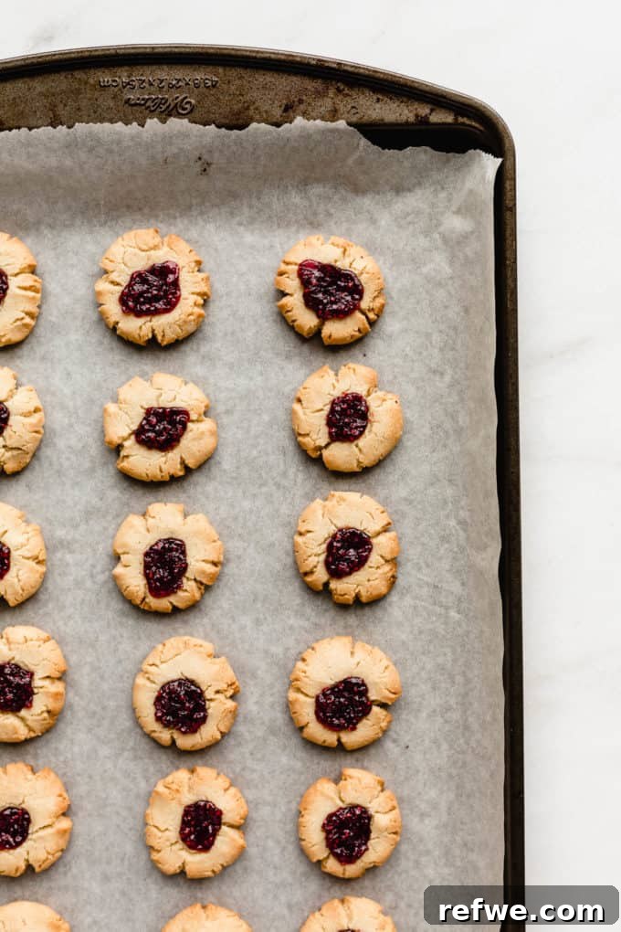 A baking pan filled with freshly baked raspberry thumbprint cookies, their golden edges and shimmering jam inviting a taste.