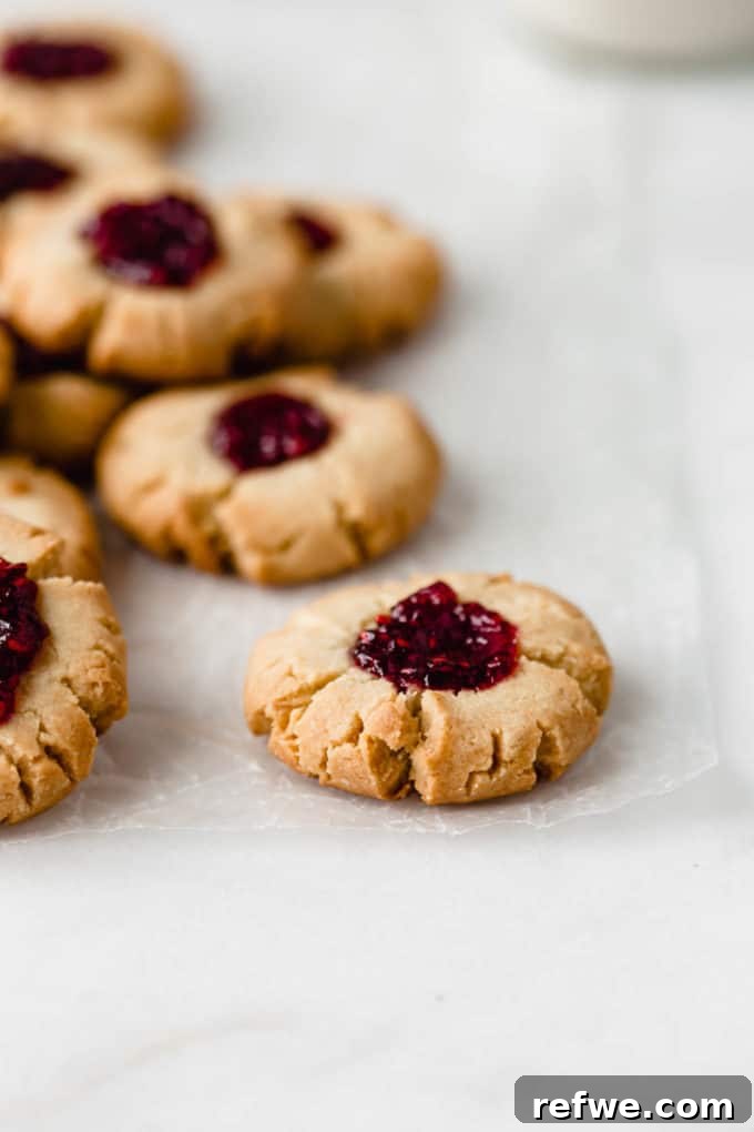 A delightful pile of baked raspberry thumbprint cookies artfully arranged on a piece of wax paper, ready to be enjoyed.