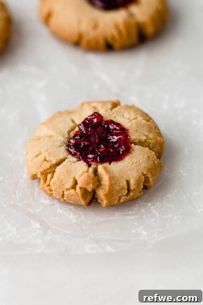 A single vegan raspberry thumbprint cookie beautifully presented on a piece of wax paper, highlighting its detailed texture and inviting appearance.
