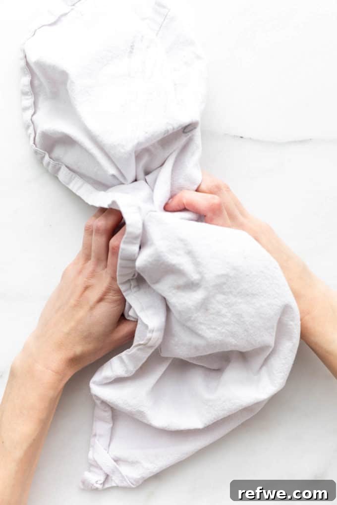 Plant-Based Hazelnut Cacao Dream 5 Two hands holding a dish towel filled with roasted hazelnuts, ready for skin removal.