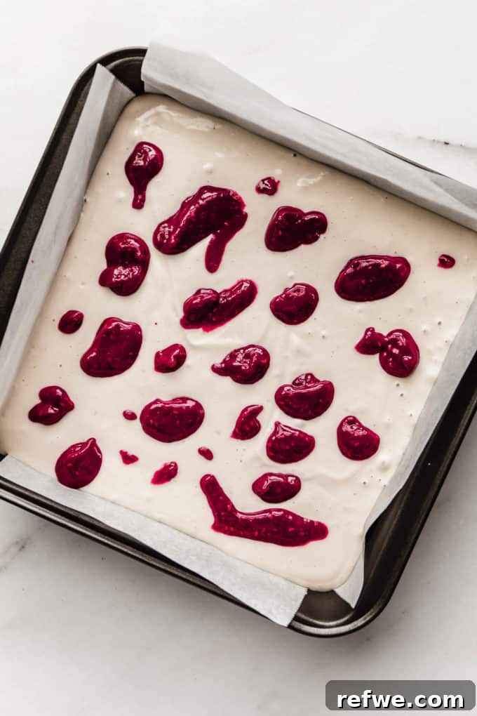 Decadent Vegan Raspberry Cheesecake Bars 10 A pan with vegan cheesecake and dollops of raspberry puree on top, ready for swirling