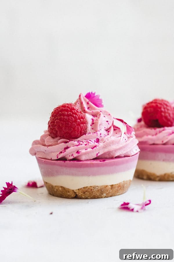 A stack of two raw vegan raspberry cheesecakes on a wooden surface, with a bite taken from the top one, revealing the creamy interior.