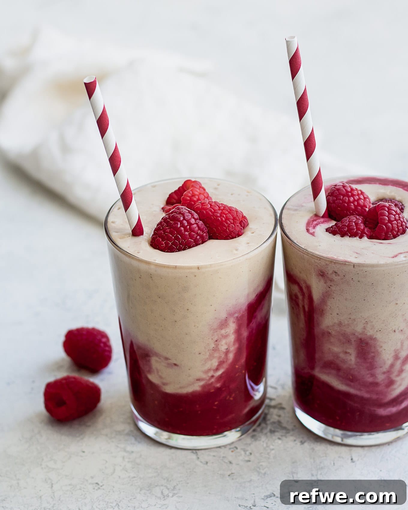Berry Peanut Butter Bliss 2 Two glasses of vibrant layered peanut butter and jelly smoothies, garnished with fresh raspberries on top.