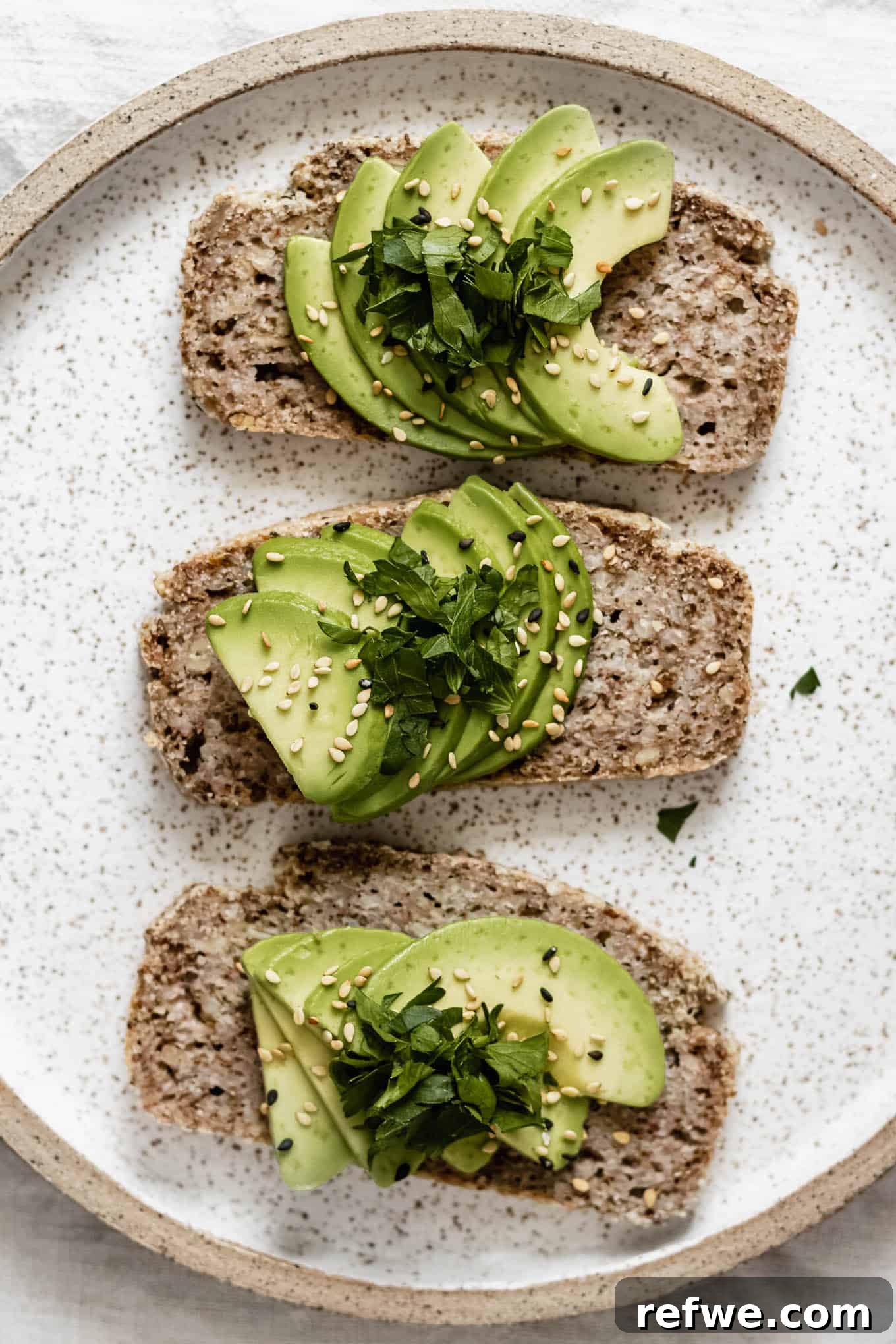 Wholesome Chia Buckwheat Loaf 11 Three perfectly presented slices of avocado toast on buckwheat bread, arranged on a white ceramic plate with a sprig of fresh herbs, emphasizing the bread's delightful texture.