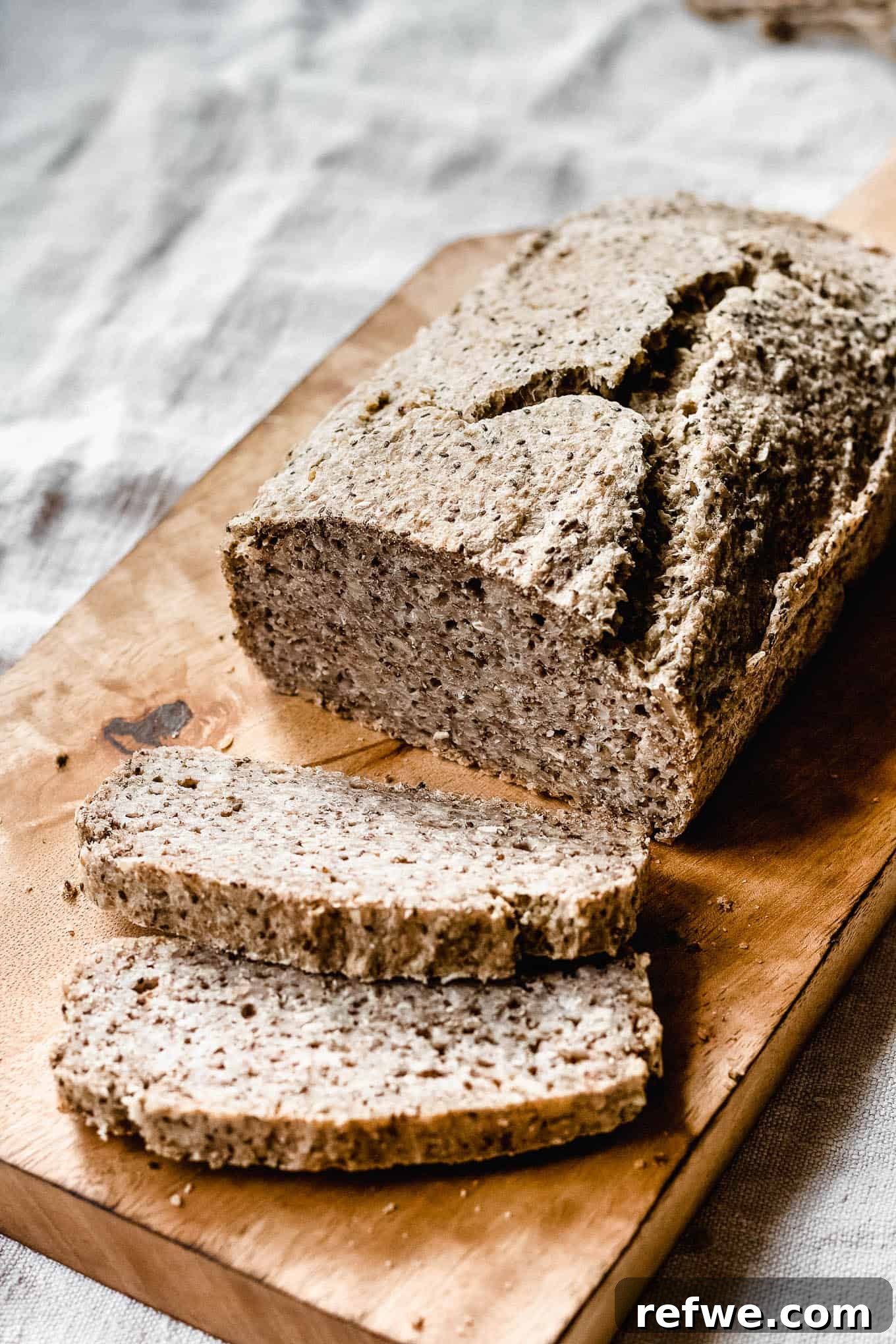 Wholesome Chia Buckwheat Loaf 9 A beautifully baked loaf of buckwheat and chia seed bread rests on a wooden bread board, inviting a perfect slice.