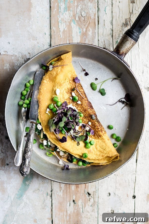 Vibrant Vegan & Gluten-Free Chickpea Omelette with Spinach and Spring Peas 3 Close-up of a vegan and gluten-free chickpea omelette in a skillet, ready to be served with a knife and fork, showcasing its appealing texture and golden-brown finish.