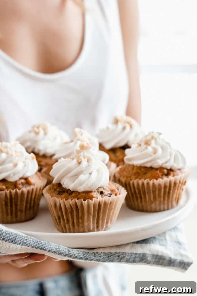 Irresistible Vegan Carrot Cupcakes 3 A hand gently reaching for a plate laden with freshly baked and frosted vegan carrot cake cupcakes, showcasing their inviting appearance.