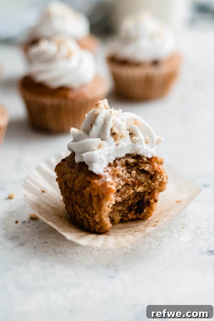 Irresistible Vegan Carrot Cupcakes 5 A close-up of a vegan carrot cake cupcake with a bite taken out, revealing its moist, spiced interior and fluffy coconut whipped cream.