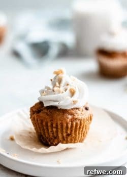 A vegan carrot cake cupcake, richly spiced and topped with a generous swirl of coconut whipped cream, garnished with crushed walnuts.