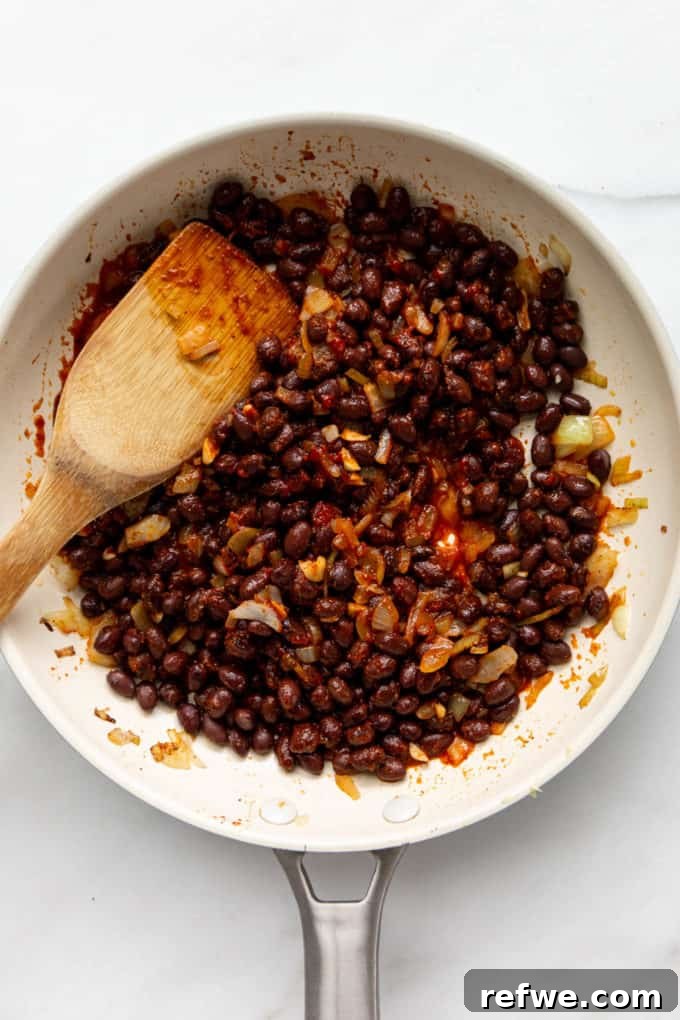 Hearty Black Bean Quinoa Stuffed Sweet Potatoes 6 Black beans coated in a rich, spicy tomato-chipotle sauce in a white pan, simmering to perfection.