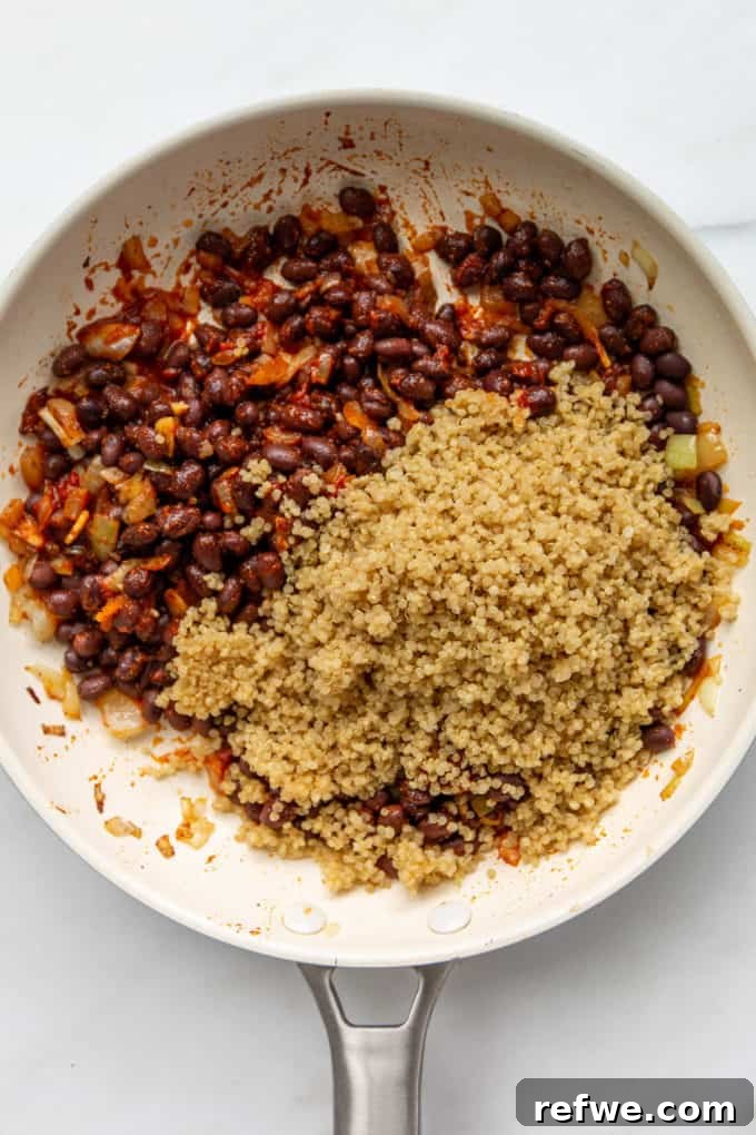 Hearty Black Bean Quinoa Stuffed Sweet Potatoes 7 A vibrant mixture of black beans and cooked quinoa being stirred in a white pan, absorbing rich flavors.