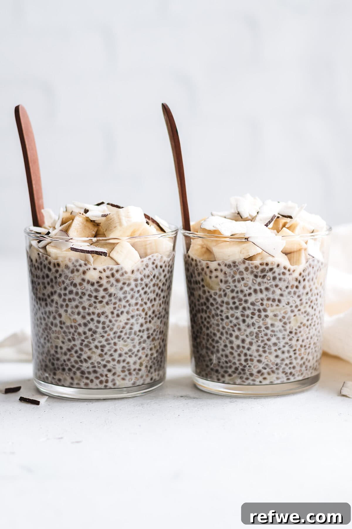 Wholesome Banana Chia Delight 2 Two cups of creamy banana chia pudding, generously topped with fresh banana slices and a sprinkle of toasted coconut flakes.