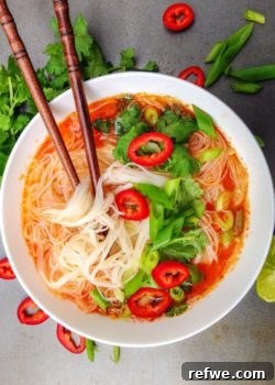 A bowl of vibrant Thai Red Curry Soup, garnished with fresh herbs and rice noodles.