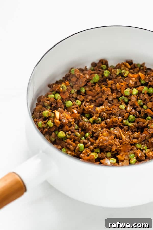 Plant-Powered Lentil Shepherd's Pie 3 A vibrant mix of lentils, green peas, and finely chopped vegetables simmering in a white pot