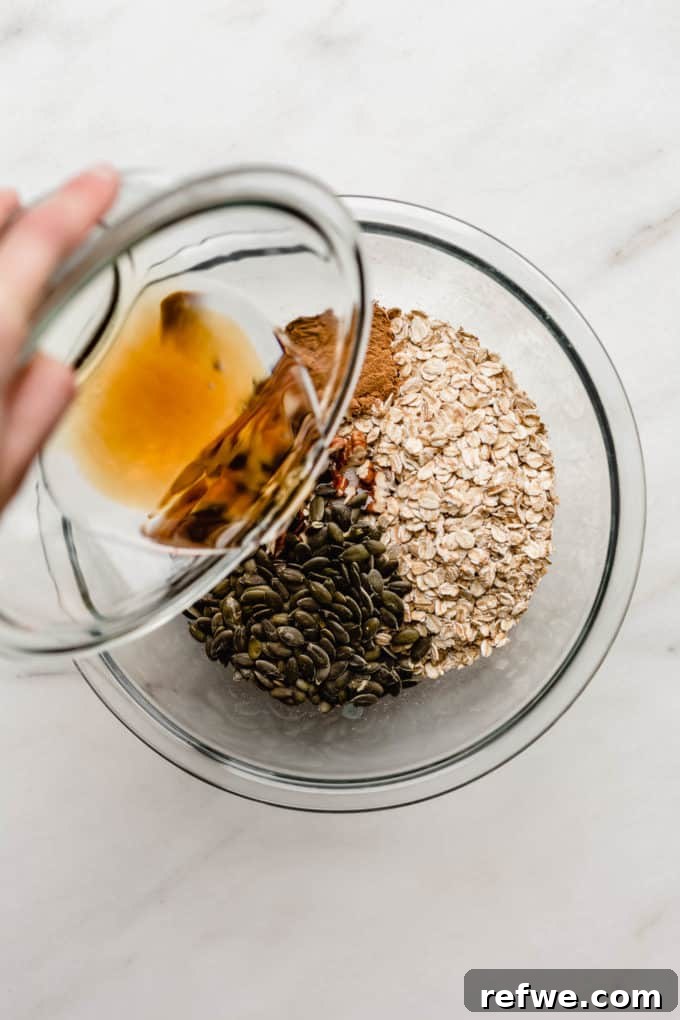 Cozy Autumn Granola 5 A hand pouring golden maple syrup into a bowl of dry granola ingredients.