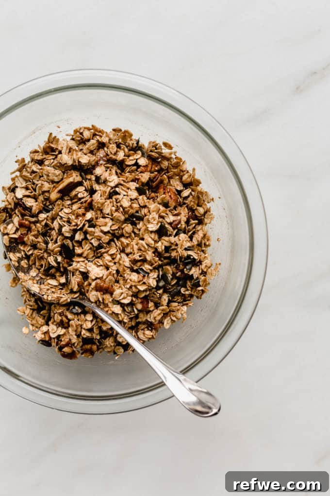 Cozy Autumn Granola 6 A clear mixing bowl brimming with freshly prepared pumpkin spice granola mixture, ready for baking.