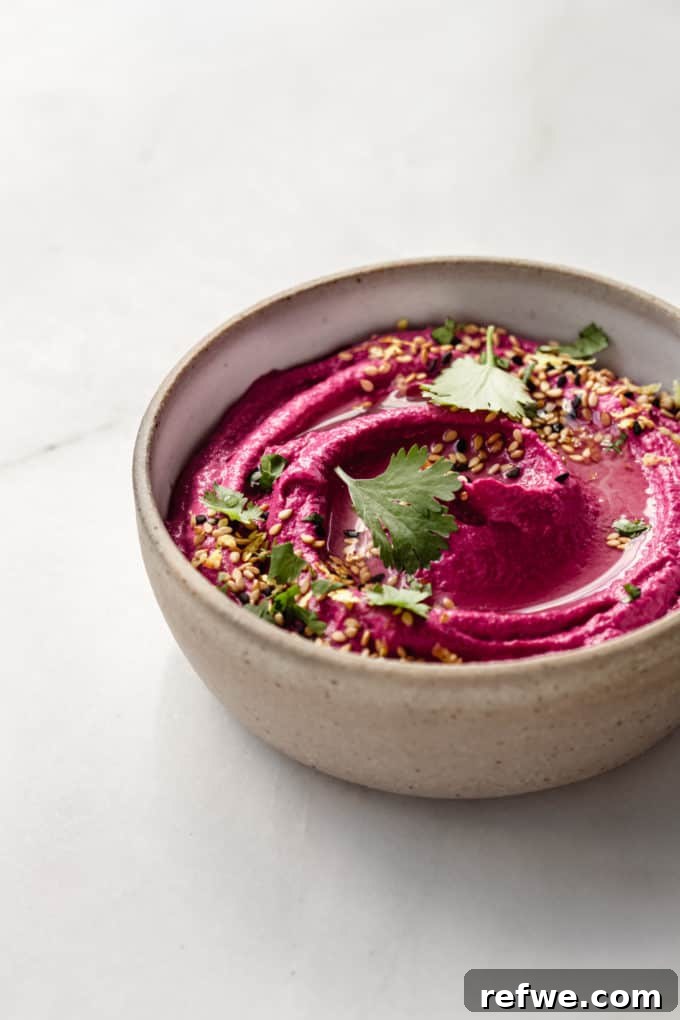 Vibrant Roasted Beet Hummus 4 A beige ceramic bowl filled with creamy beet hummus, placed on a simple background.
