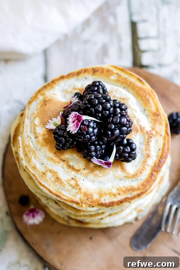 Close-up of fluffy lemon poppy seed spelt pancakes, stacked high and ready to be topped, showcasing their golden edges and delicate poppy seed speckles.