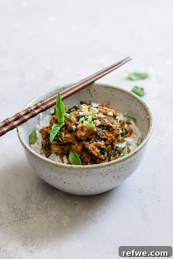 Fragrant Thai Basil Tempeh Stir-Fry 6 A close-up of a serving of Thai basil tempeh stir fry in a white bowl, garnished with fresh basil.