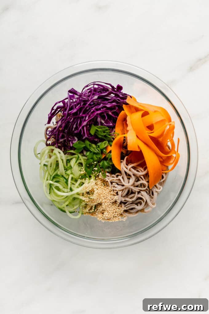 Chilled Soba Noodles with Creamy Peanut Sauce 6 A large salad bowl filled with cooked soba noodles, shredded cabbage, carrots, spiralized cucumber, chopped scallions, and a sprinkle of sesame seeds, awaiting the dressing.