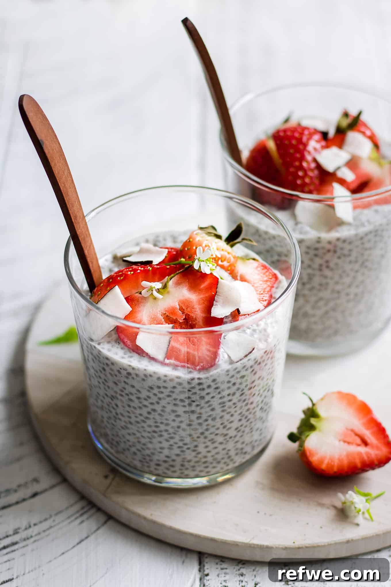 Two cups of coconut chia pudding topped with fresh strawberries on a white marble board, highlighting its vibrant and healthy appeal.