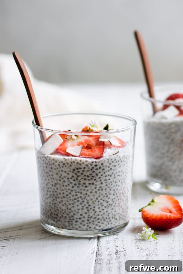 A single cup of coconut chia pudding, generously topped with vibrant strawberries and delicate flaked coconut, highlighting its appealing texture and fresh garnishes.