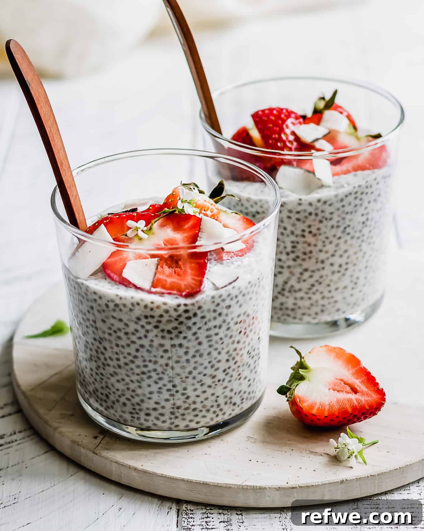 Two individual cups of coconut chia pudding, elegantly topped with fresh strawberries, showcasing a simple yet delicious presentation.