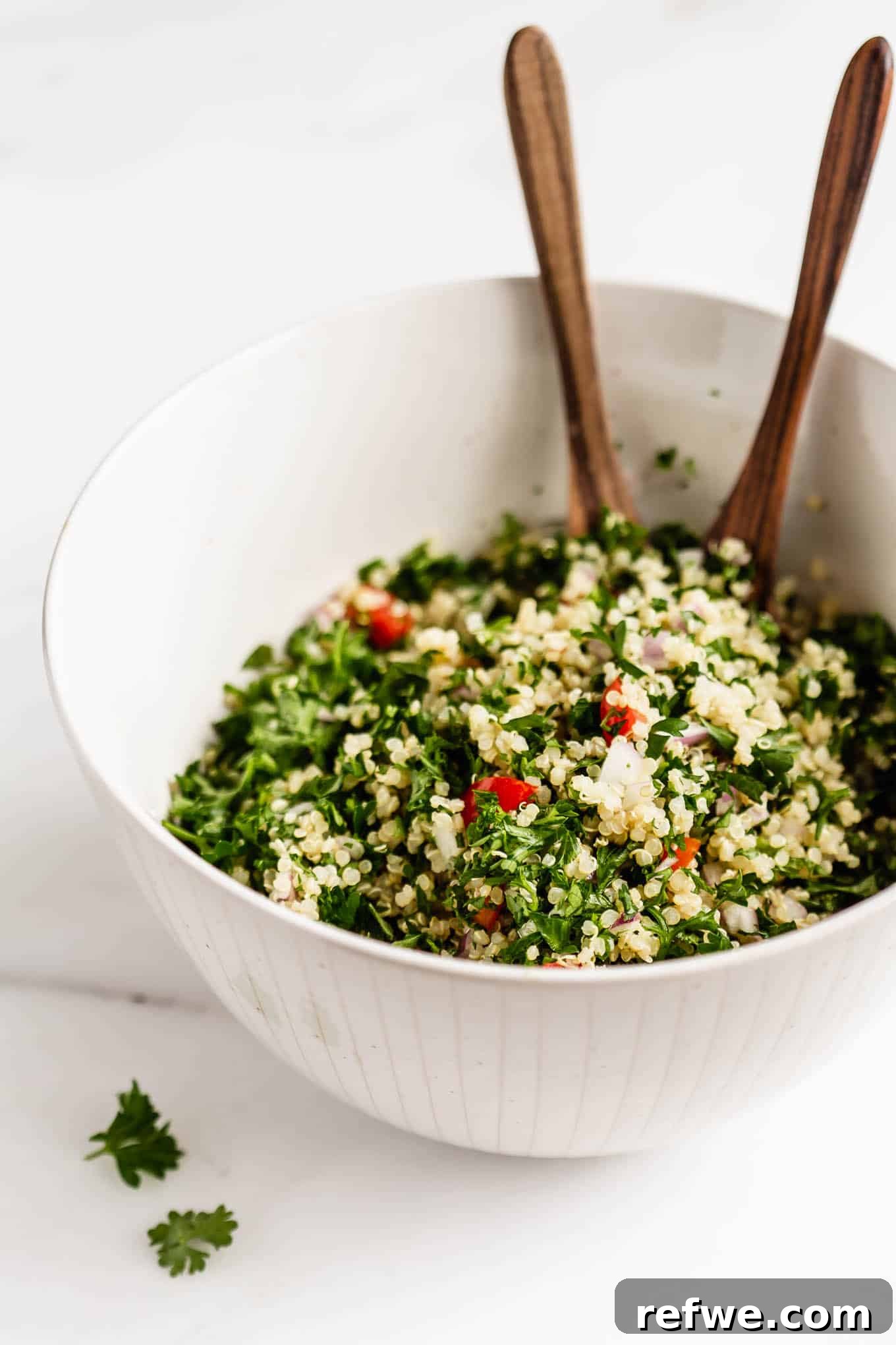 Mediterranean Quinoa Tabbouleh 2 A vibrant bowl of quinoa tabbouleh salad with wooden serving spoons, garnished with fresh mint leaves.
