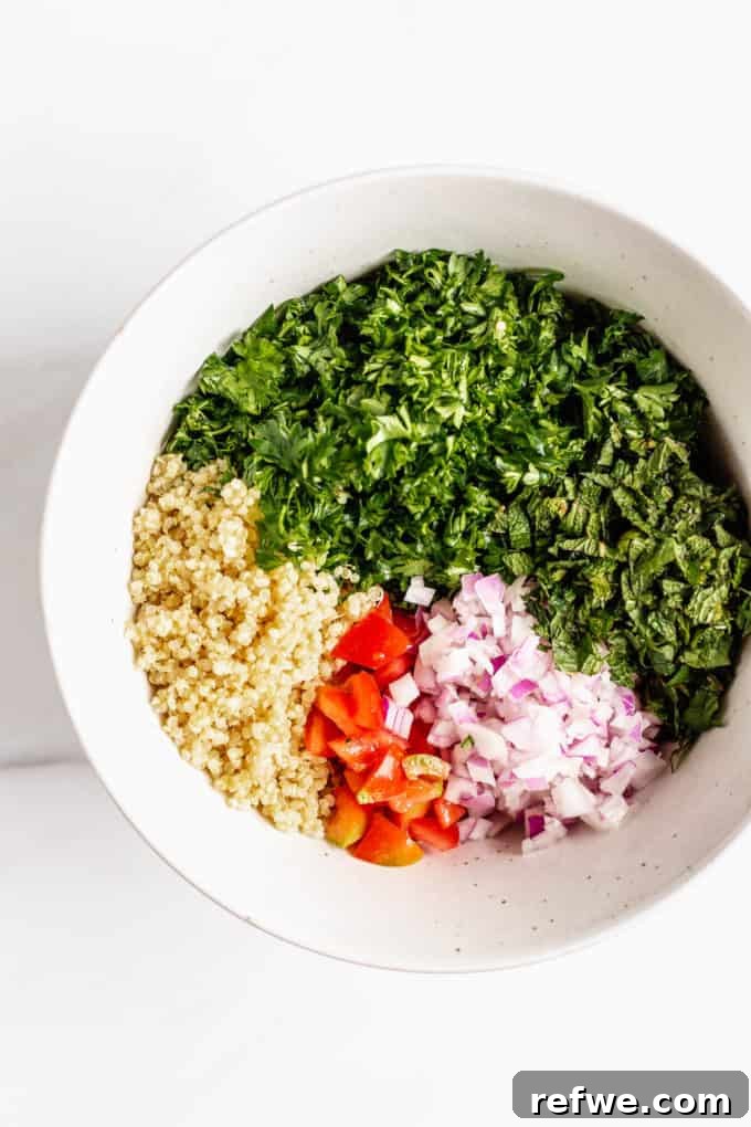 Mediterranean Quinoa Tabbouleh 4 A large mixing bowl containing cooked quinoa, finely chopped parsley, mint, red onion, and diced red bell pepper, ready to be tossed.