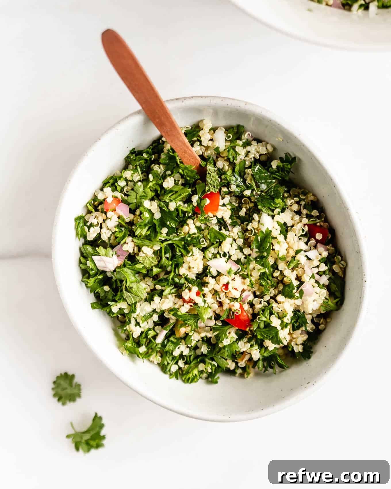 Mediterranean Quinoa Tabbouleh 6 Quinoa tabbouleh salad served in a white bowl with a wooden serving spoon, highlighting the vibrant colors and fresh ingredients.