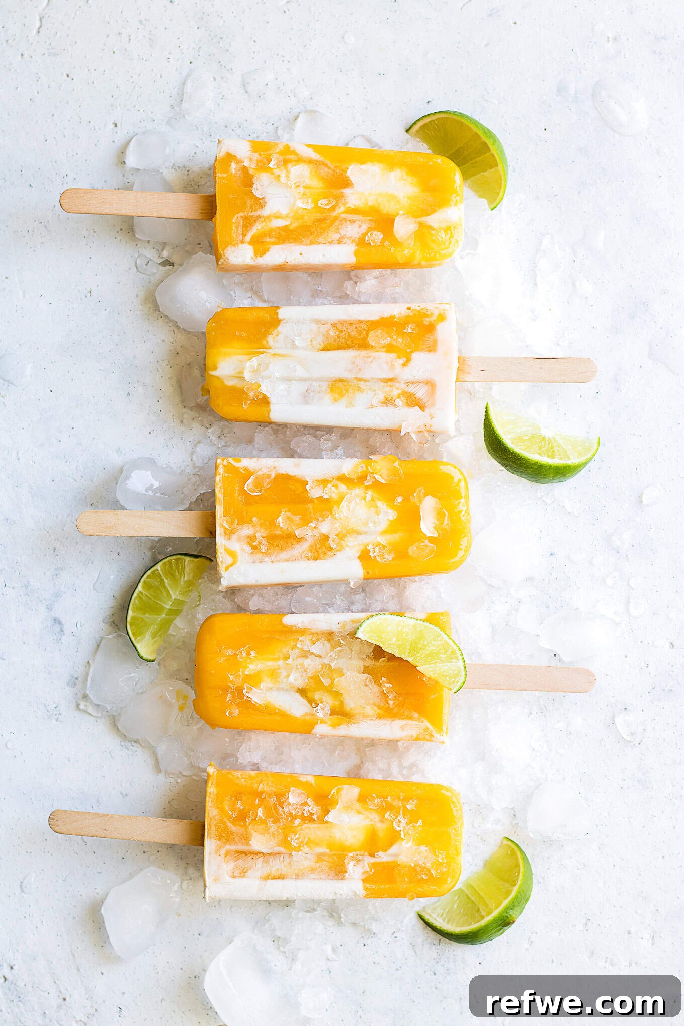 Creamy Mango Lassi Pops 4 Rows of perfectly frozen vegan mango lassi popsicles, standing upright next to vibrant green limes, showcasing their readiness to be enjoyed.