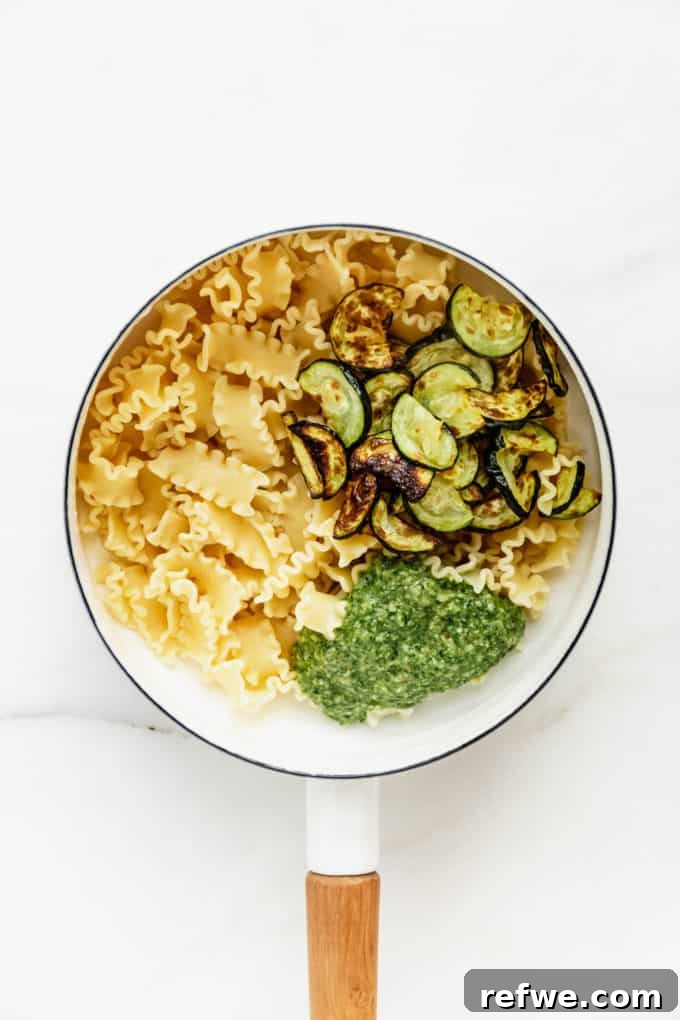Zesty Pesto Veggie Medley 5 Cooked pasta, perfectly roasted zucchini, and a dollop of vibrant pesto awaiting a good stir in a white pot
