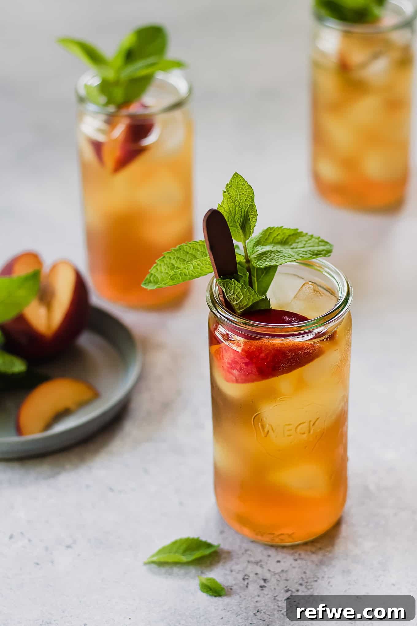 Peach Cold Brew Refresher 4 A glass of cold brew peach iced tea, garnished with fresh peaches and mint leaves.