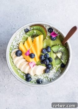 Superfood green smoothie bowl garnished with fresh fruit and coconut